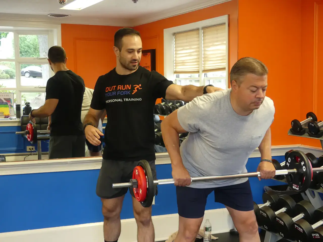 A trainer coaching a member through a dumbbell row